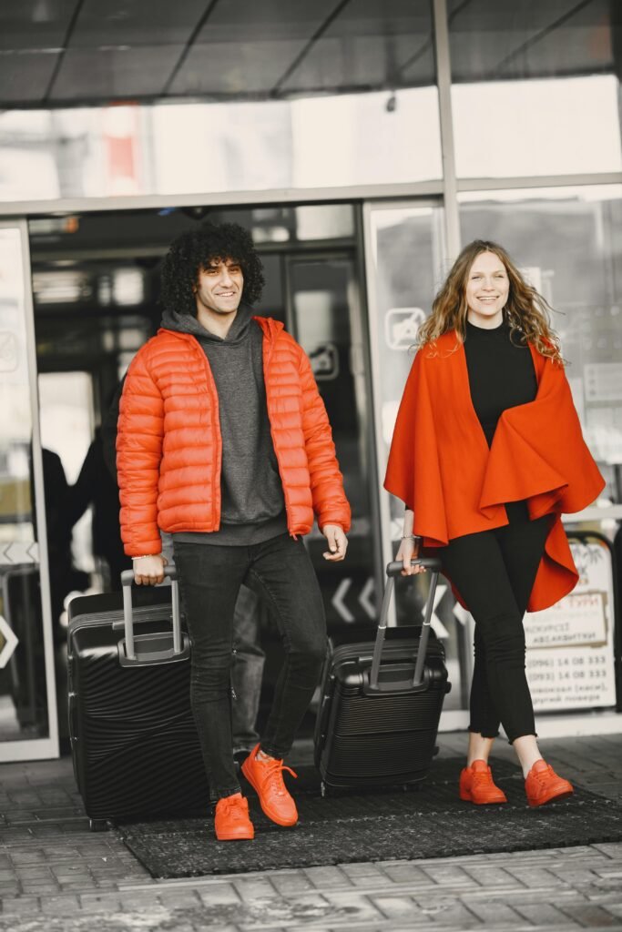 A cheerful couple exiting an airport terminal with luggage, dressed in matching red outfits.