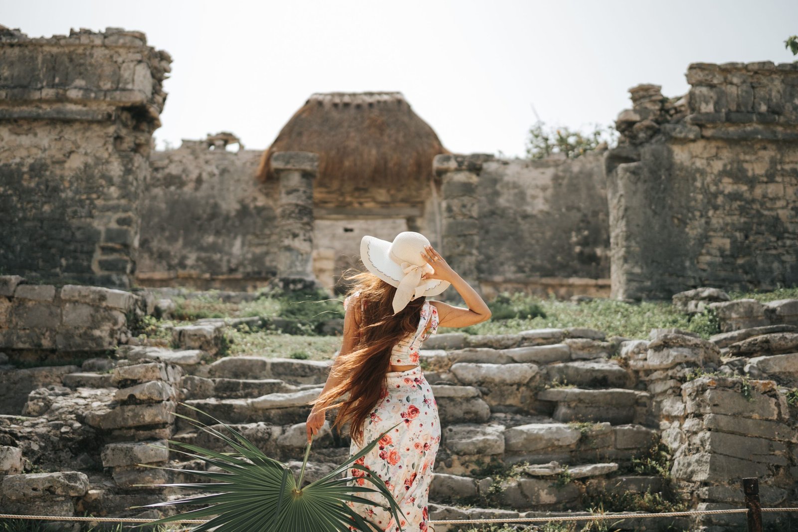 Where I’d Stay in Tulum (Boutique Luxury Without the Price) A woman in a floral dress explores the ancient Tulum ruins in Mexico during summer.