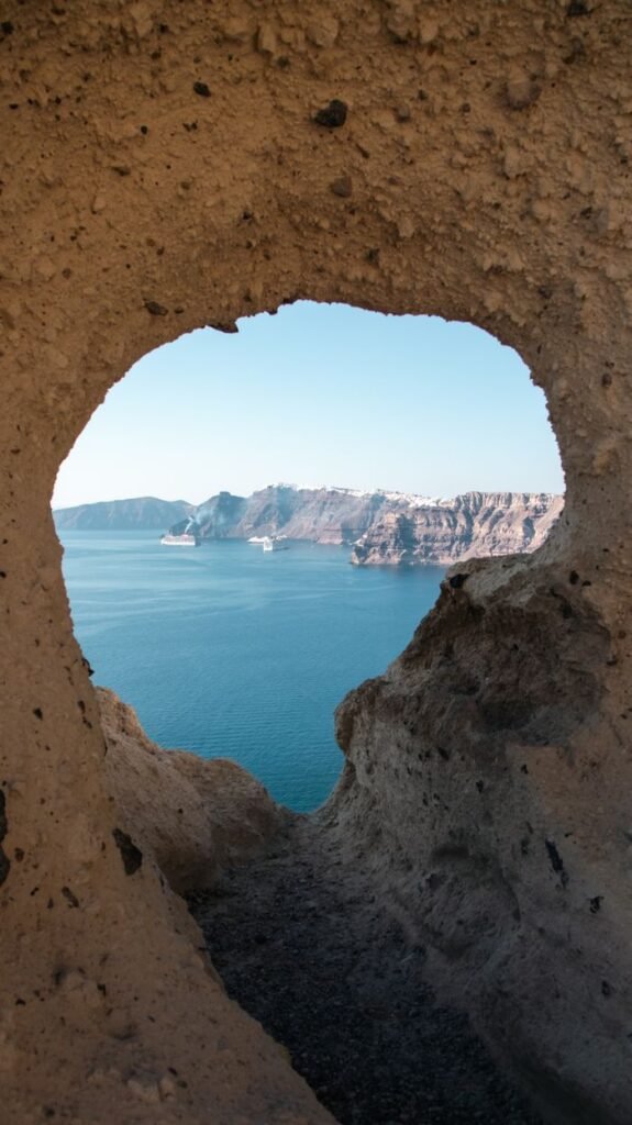 pexels photo 33554181 33554181 Scenic view of Santorini's cliffs and sea through a natural cave opening, capturing Greece's stunning landscape.