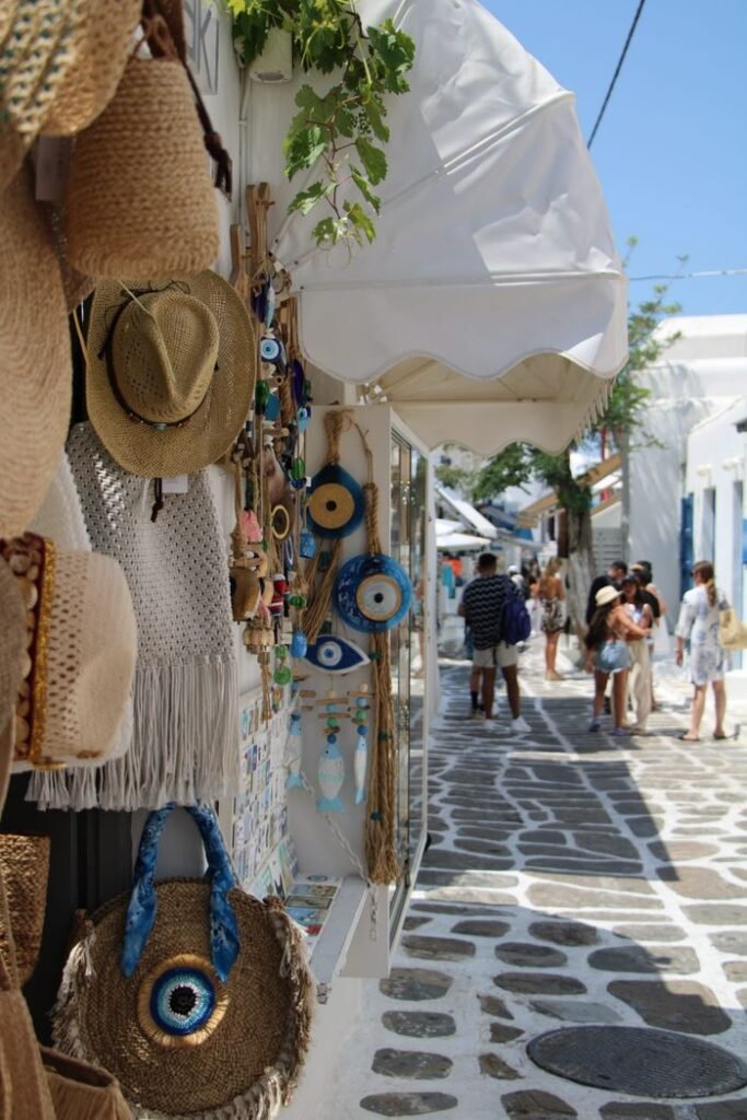 pexels photo 36597484 36597484 Explore a sunlit Mykonos street lined with charming boutiques and traditional whitewashed buildings.