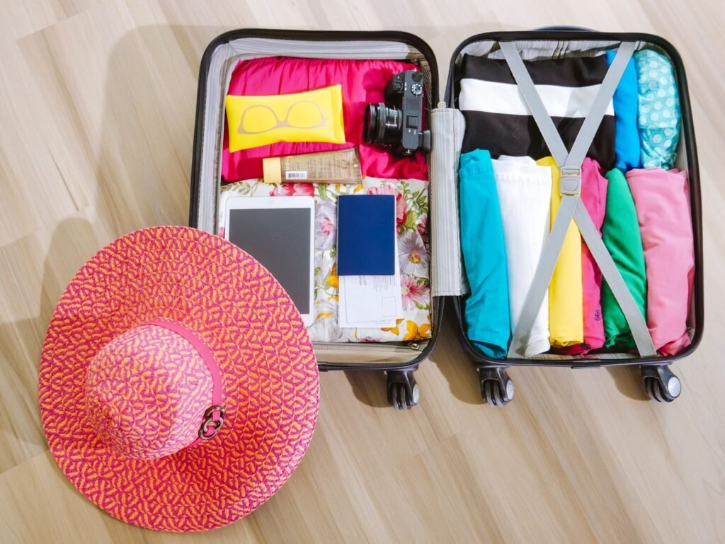pexels photo 8212231 8212231 Top view of a suitcase packed with clothes, a camera, and a sun hat, ready for summer travel.